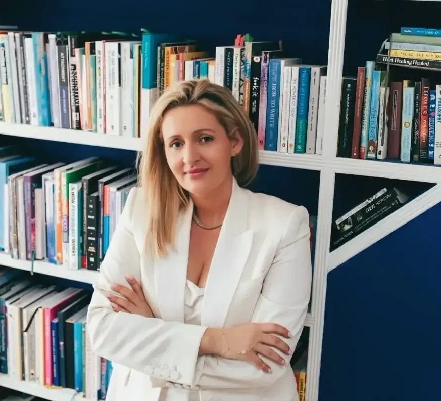 Confident woman standing in front of a bookshelf filled with mental health books