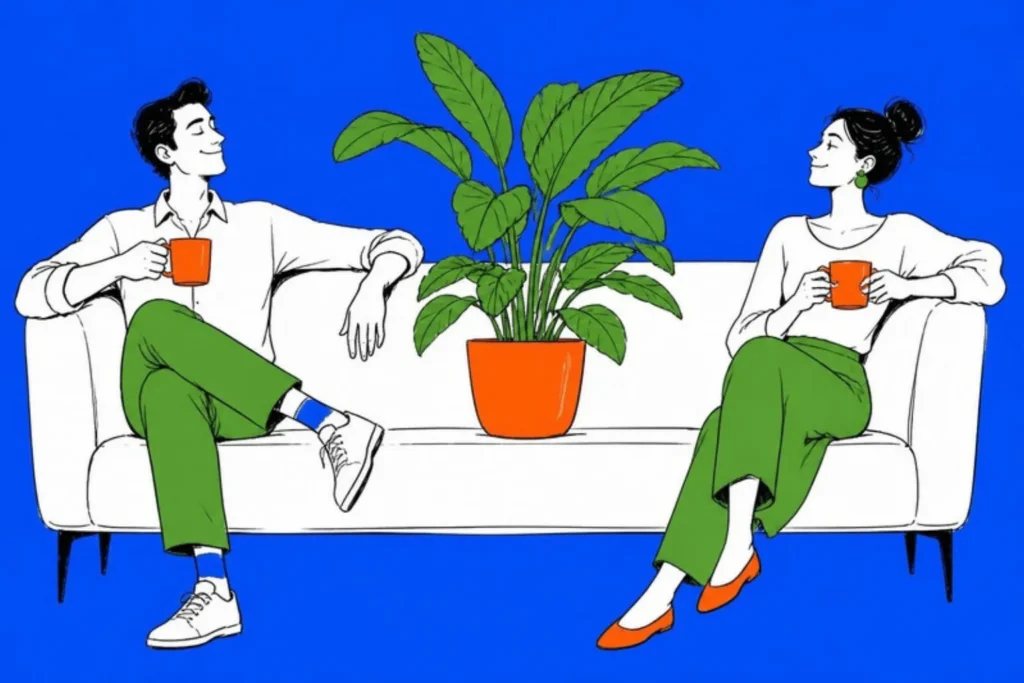 Two adults at opposite ends of a sofa with mugs and a large plant between them, cobalt background